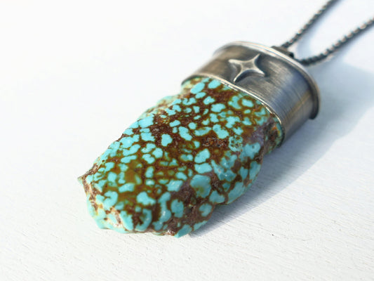 Kingman turquoise nugget pendant with dark oxidized sterling silver setting and black chain, featuring polished and rough turquoise surfaces.
