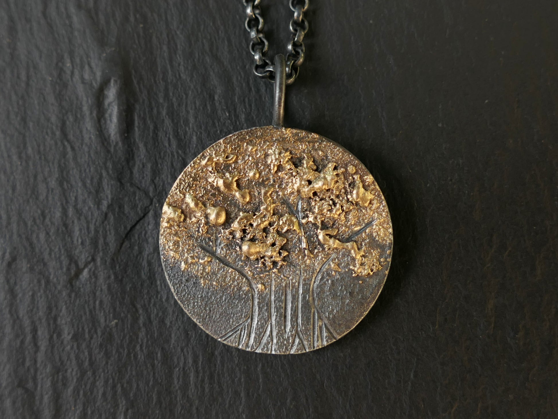 Hand engraved tree of life pendant in darkened silver with molten 14k gold details on black chain