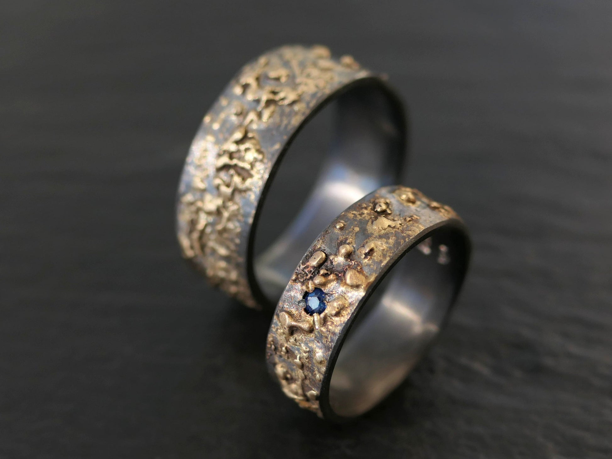 gold and black silver wedding ring set with blue sapphire gemstone and textured fire-forged surface
