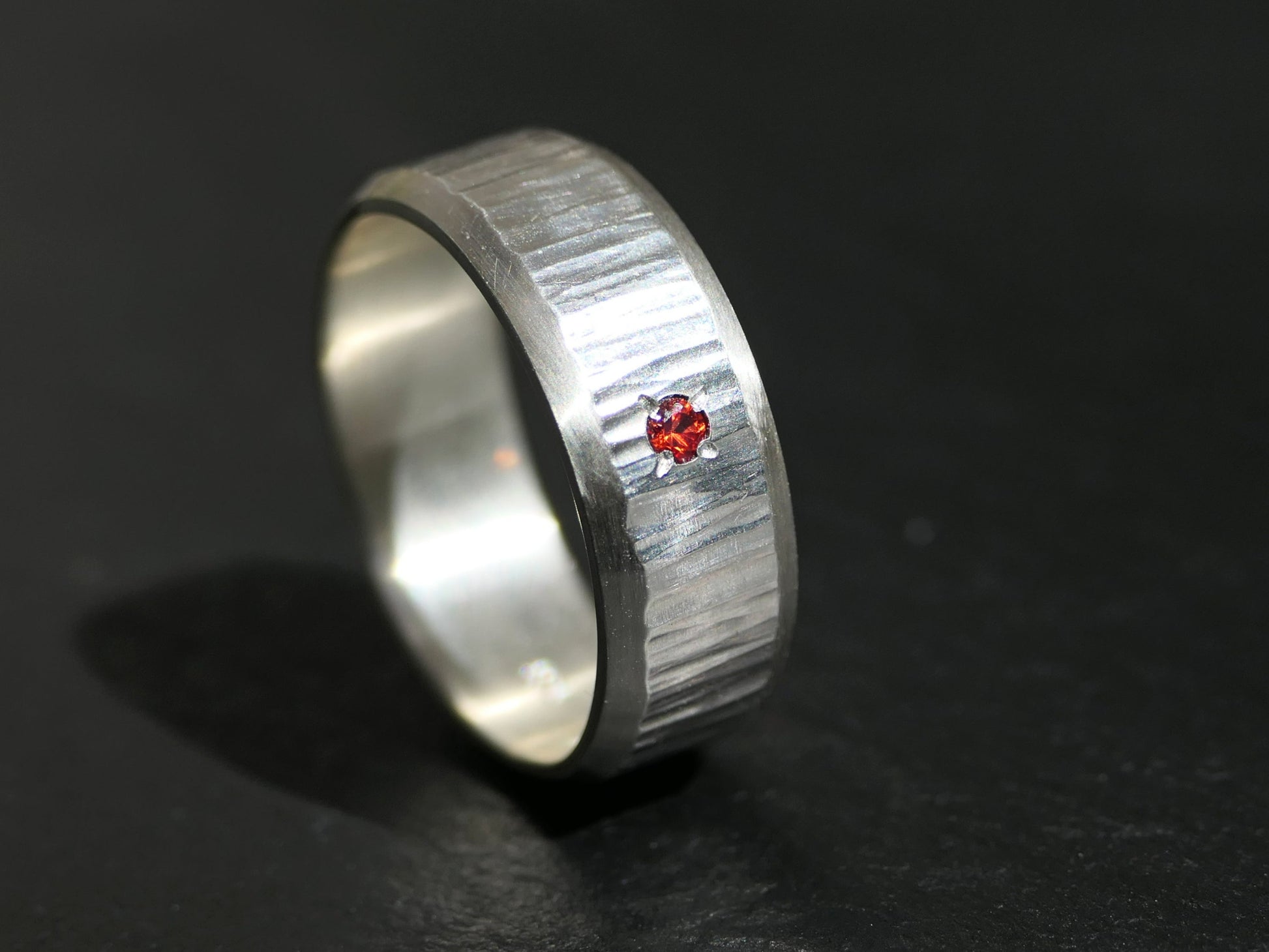 hammered sterling silver wedding band with small red gemstone on black background