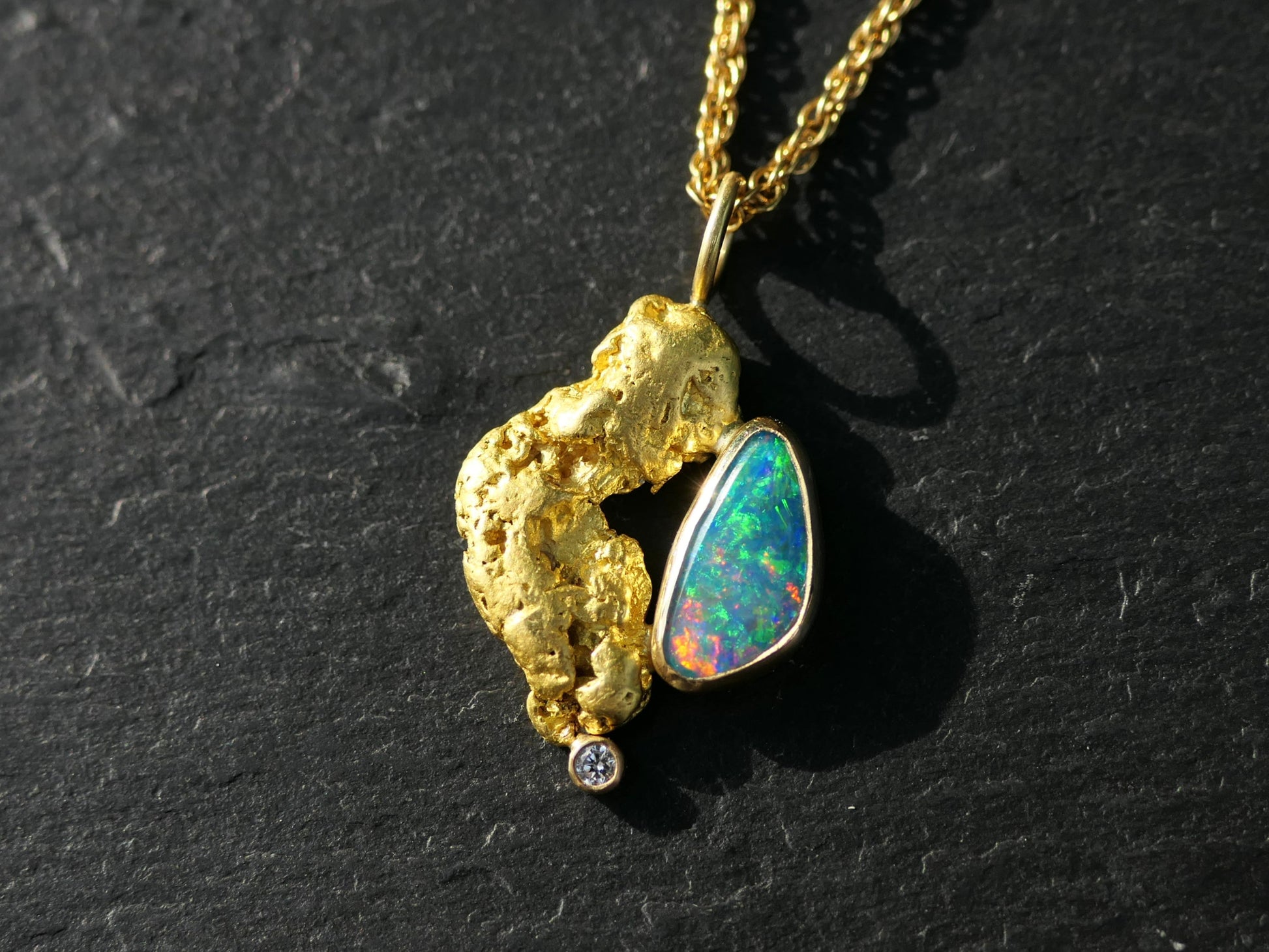 Boulder opal and gold nugget pendant with diamond accent on black background.