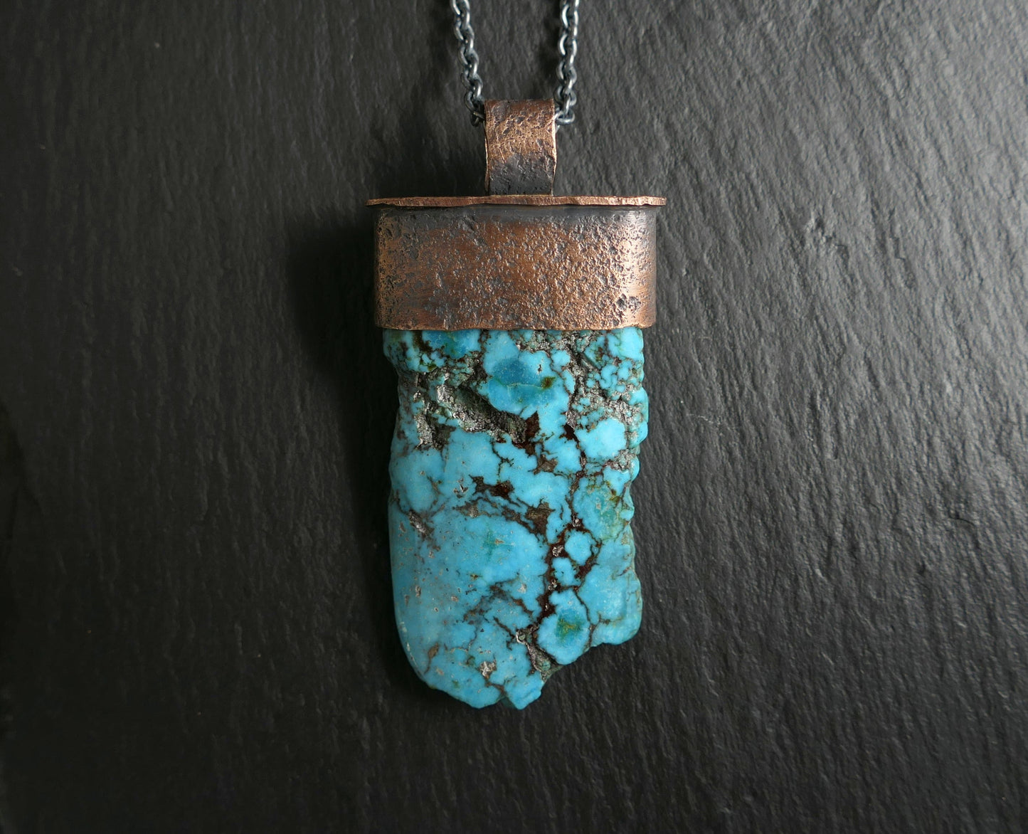 large Kingman turquoise pendant with oxidized bronze setting and black chain on dark background