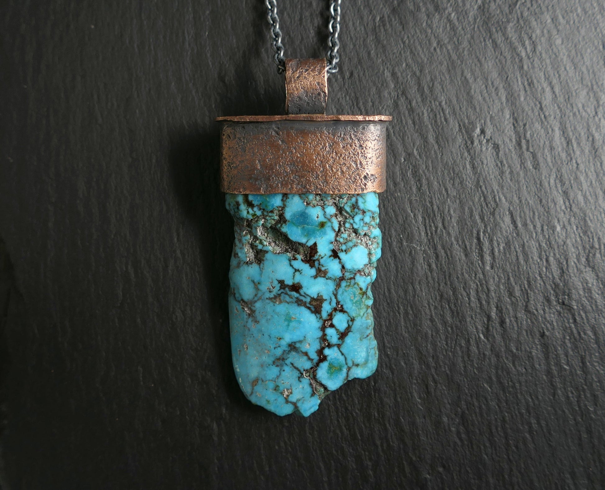 large Kingman turquoise pendant with oxidized bronze setting and black chain on dark background