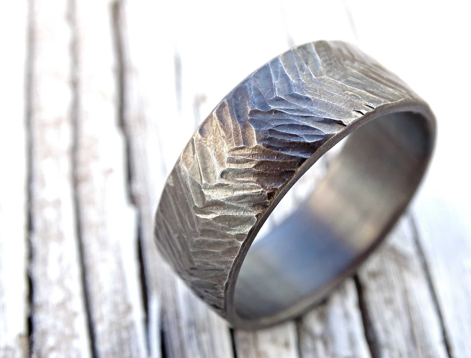 Handmade hammered silver chevron ring with textured surface and rounded inner edges on wooden background