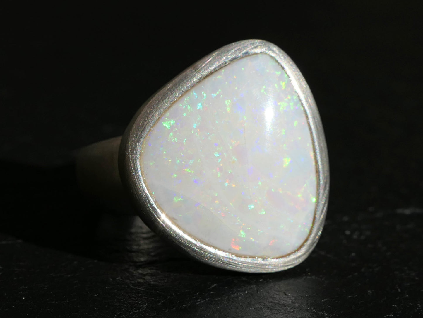 Adjustable sterling silver ring with natural Australian white opal showing green, yellow, and orange flickers in a bezel setting