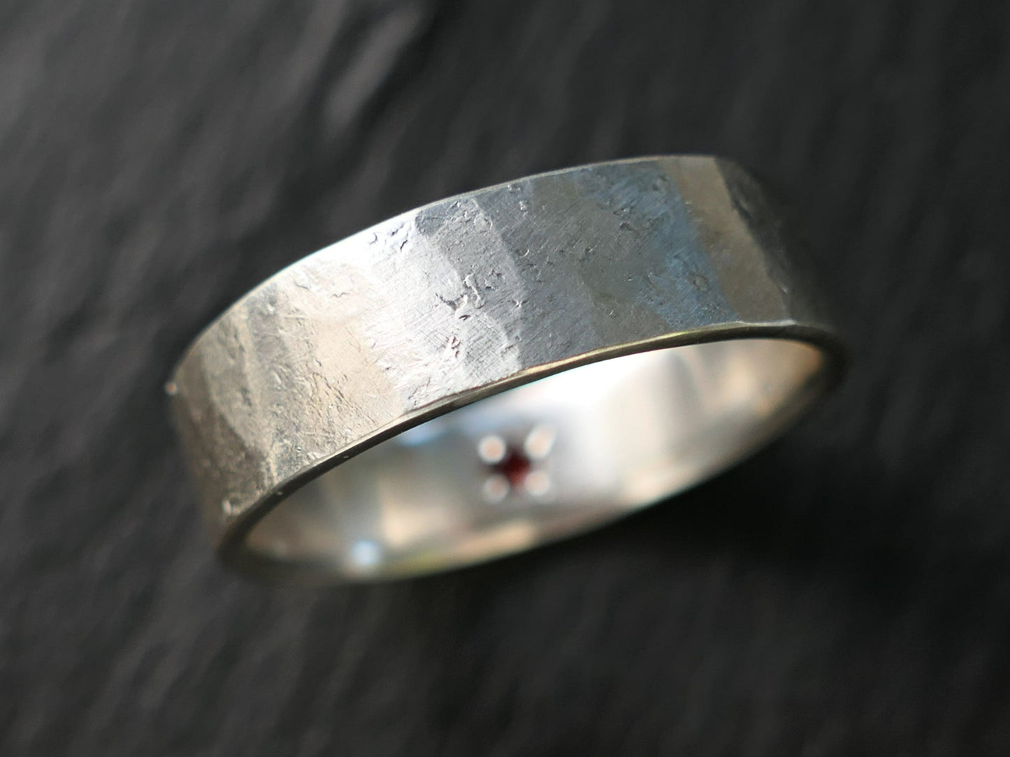 Hammered sterling silver ring with a hidden red gemstone set inside the band, matte brushed finish, durable and handcrafted.