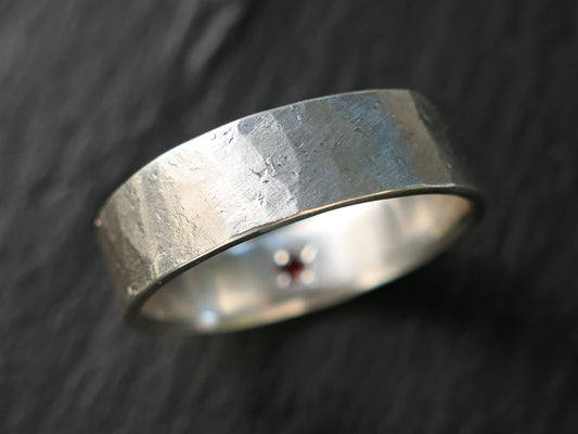 Hammered sterling silver ring with a hidden red gemstone set inside the band, matte brushed finish, durable and handcrafted.