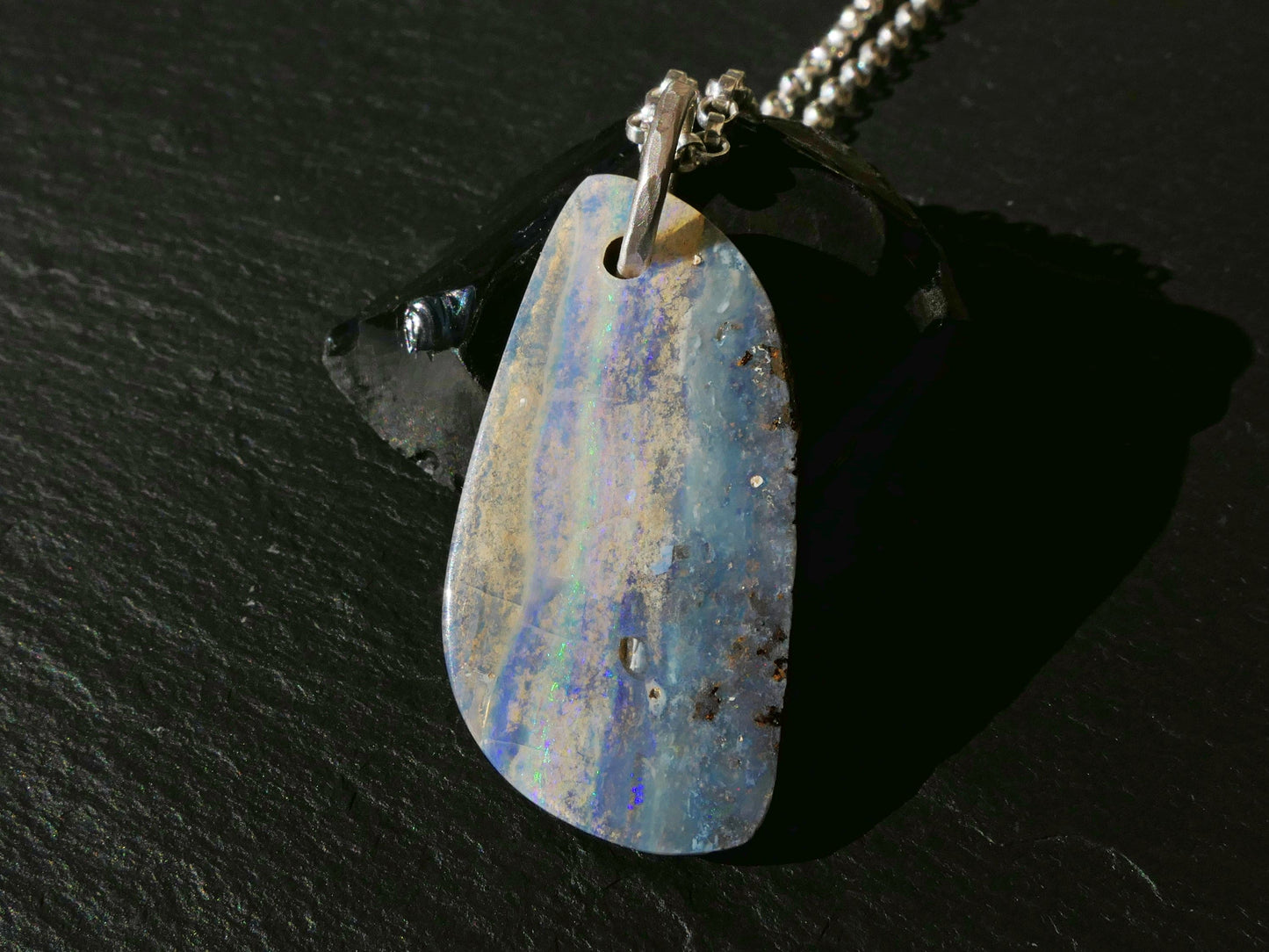 Multi-colored Australian boulder opal pendant necklace with sterling silver bail on black surface