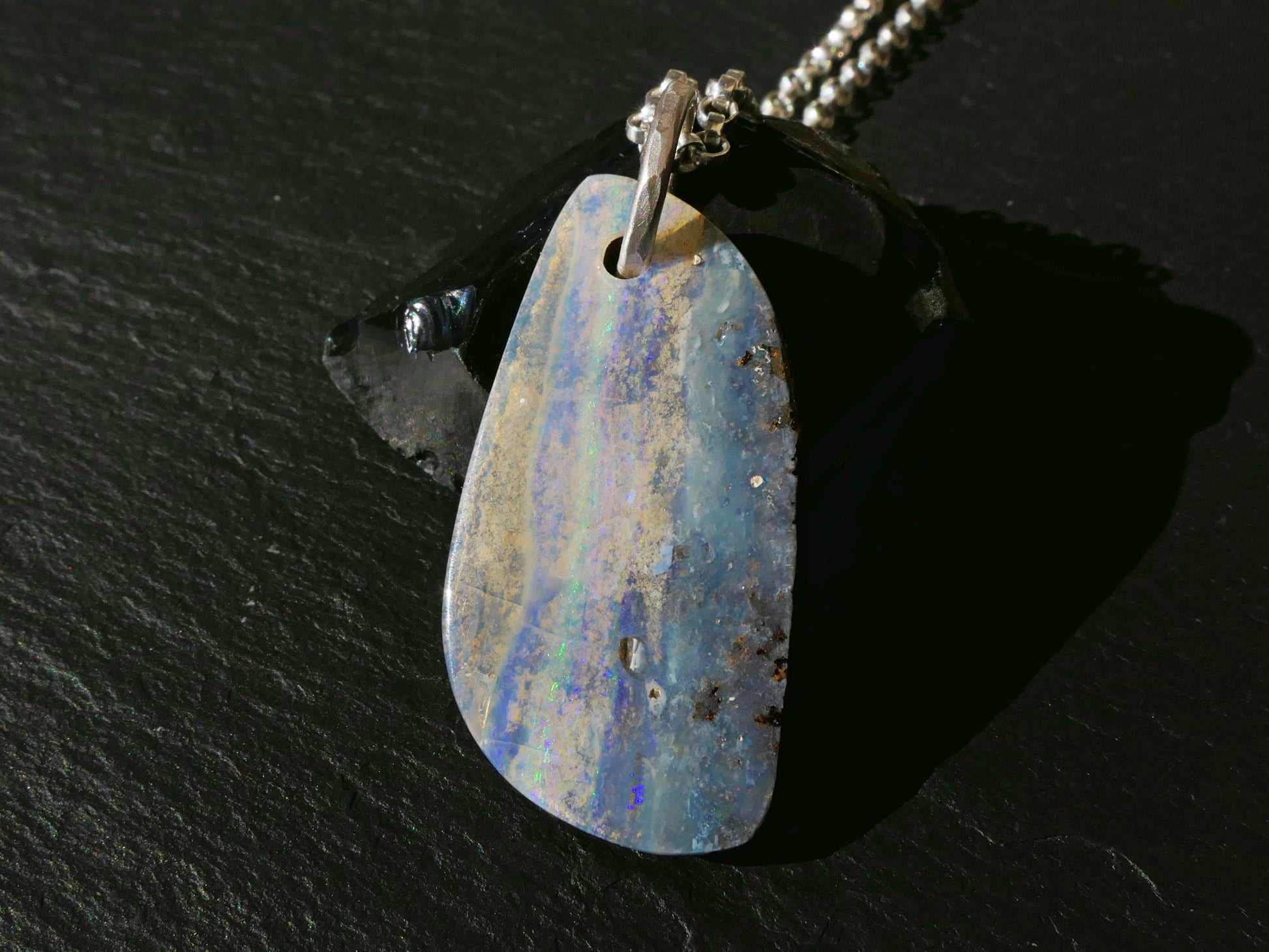Multi-colored Australian boulder opal pendant necklace with sterling silver bail on black surface