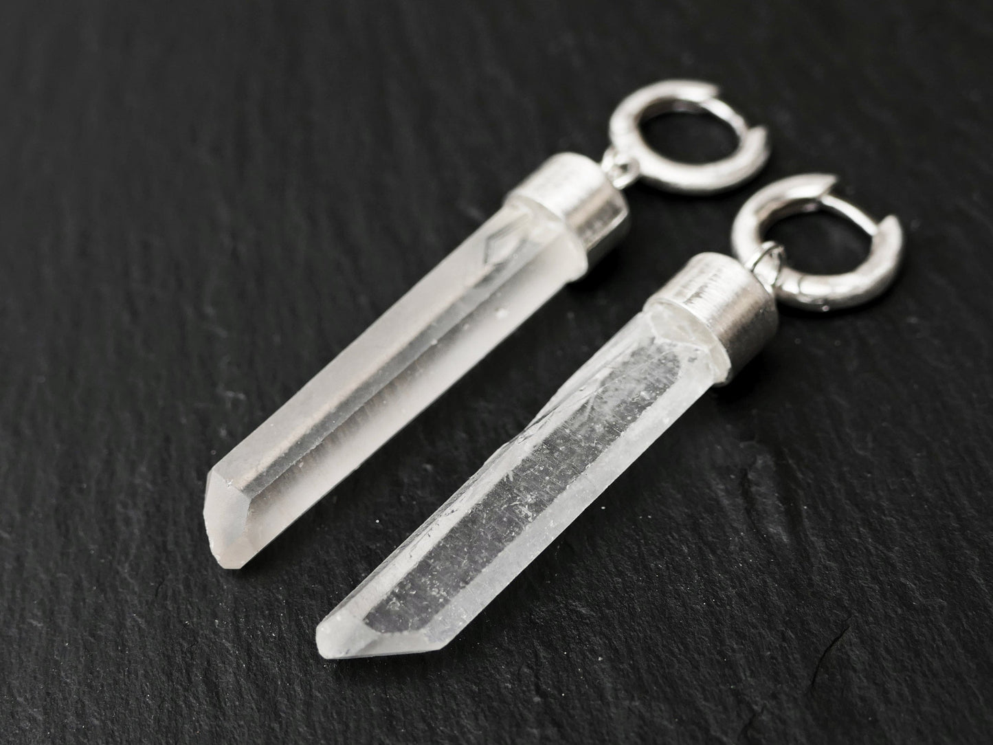 Sterling silver huggie earrings with natural raw quartz crystal dangles on a black background