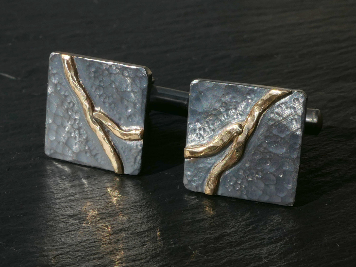 Handforged dark oxidized sterling silver cuff links with hammered texture and solid 14k gold river design.