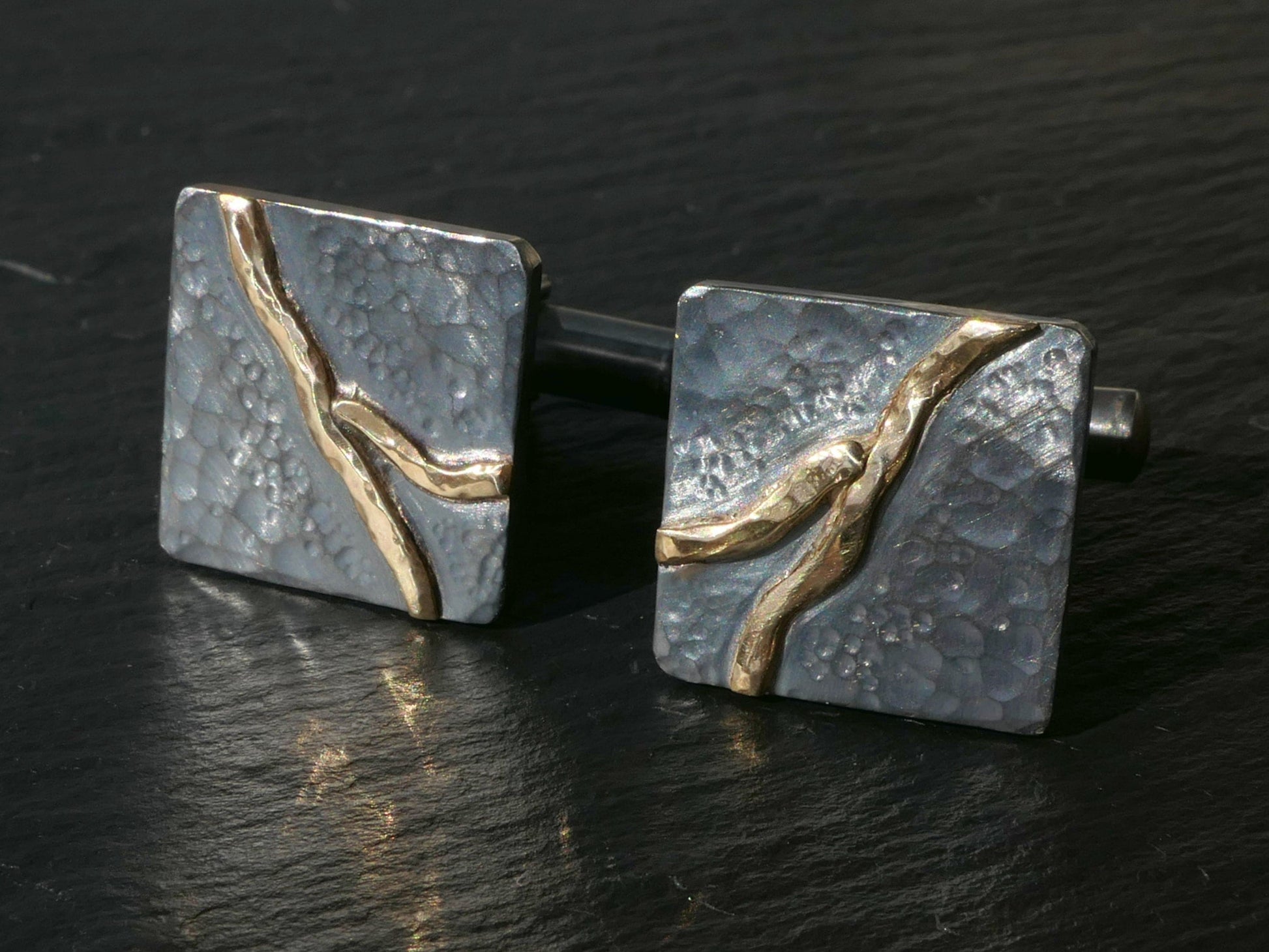 Handforged dark oxidized sterling silver cuff links with hammered texture and solid 14k gold river design.