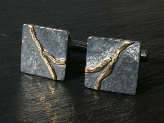 Handforged dark oxidized sterling silver cuff links with hammered texture and solid 14k gold river design.