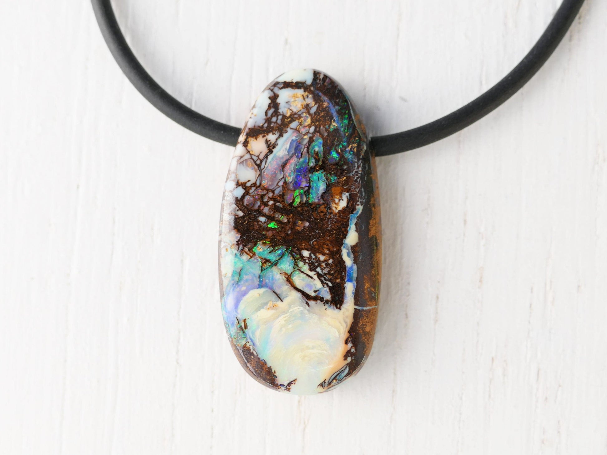 Close-up of a polished opalized wood boulder opal pendant on a black neoprene cord necklace