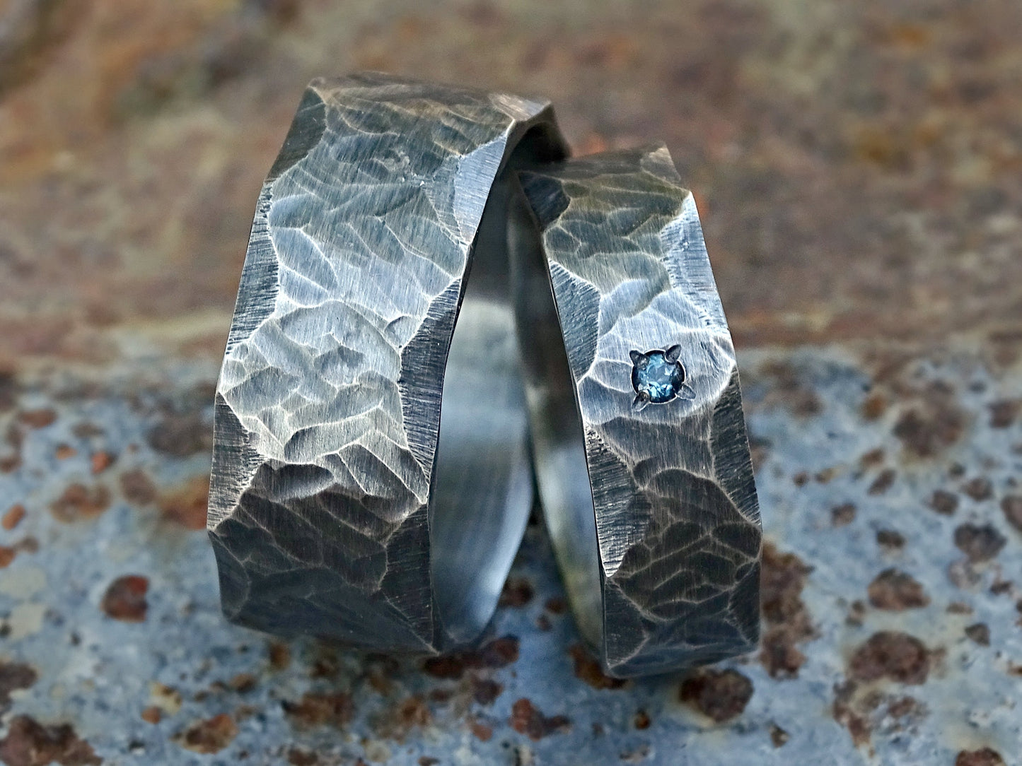 hand forged matching sterling silver wedding bands with hammered texture and small blue gemstone on slimmer ring