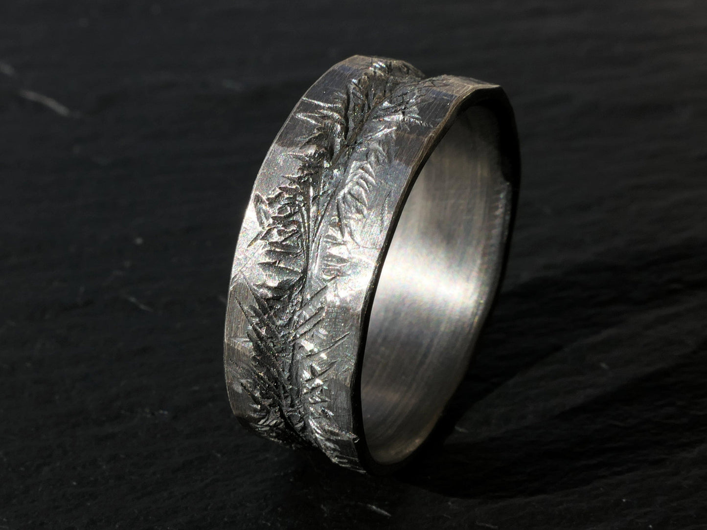 dark silver carved mens wedding band with textured hand carved center and slightly uneven edges on black background