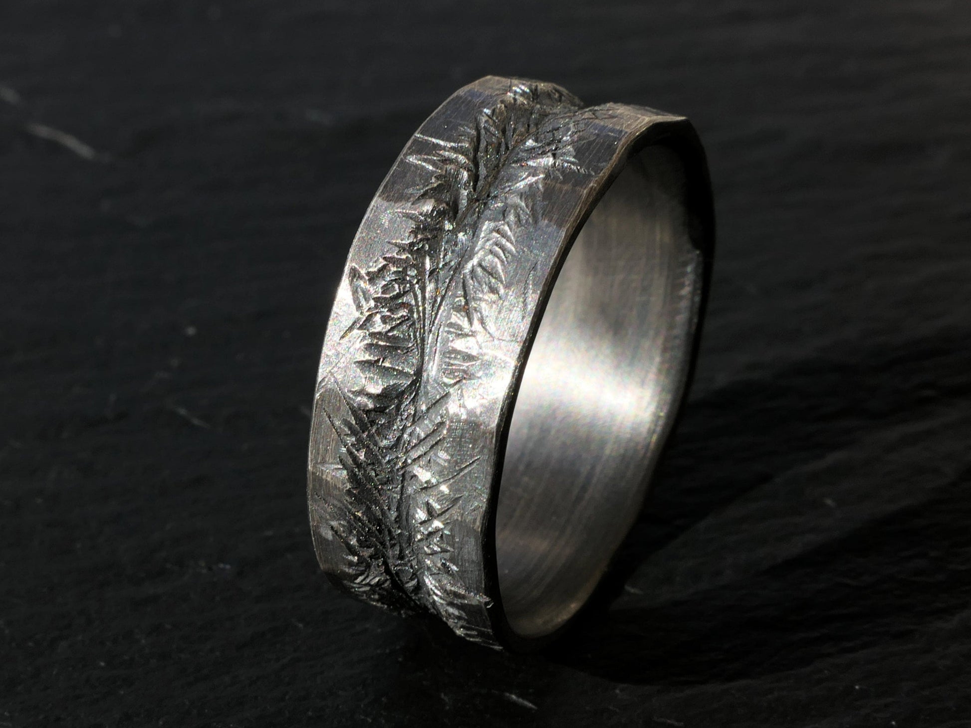 dark silver carved mens wedding band with textured hand carved center and slightly uneven edges on black background