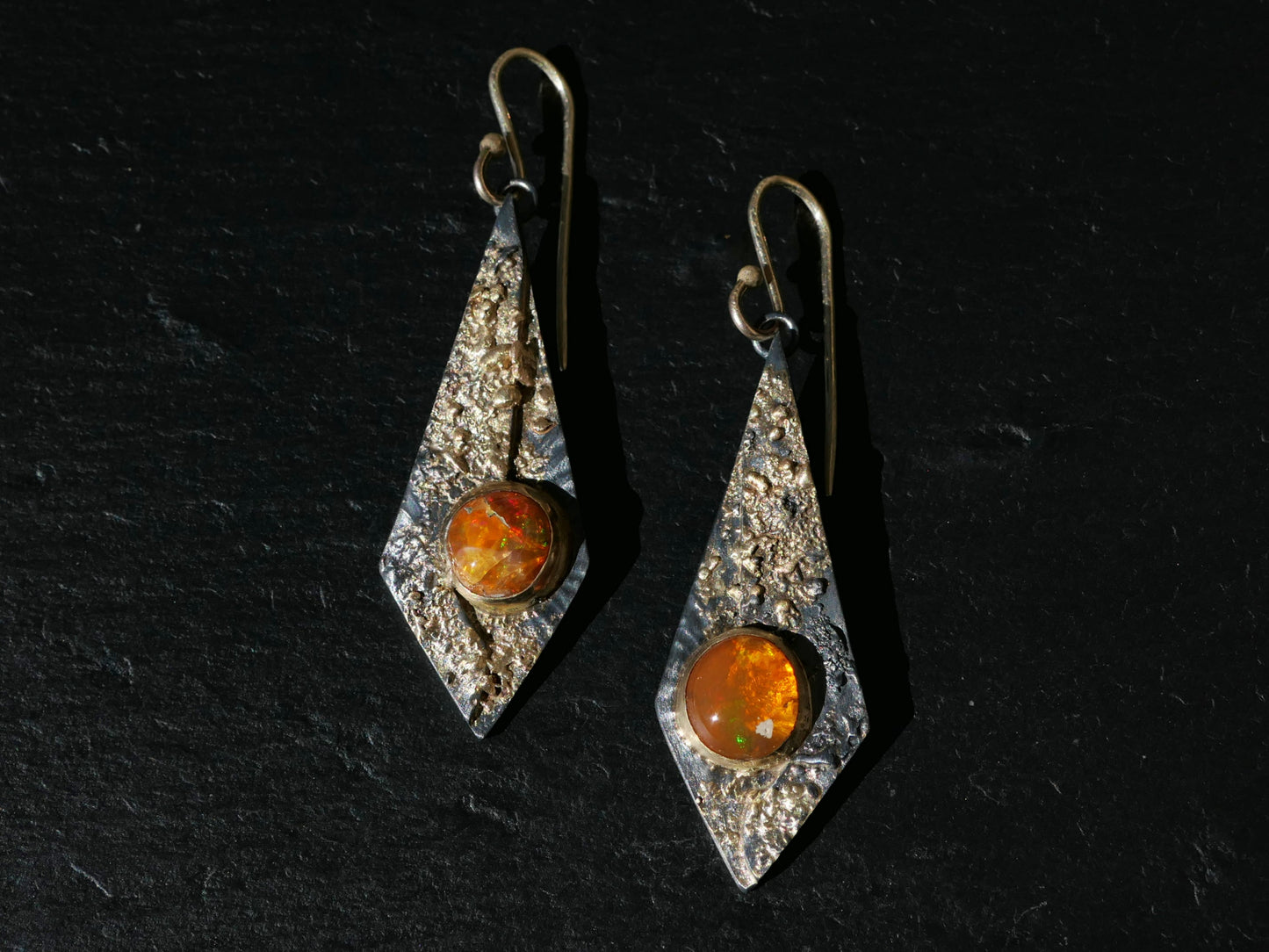 Kite-shaped statement earrings with orange Mexican fire opal gemstones set in textured 14k gold and black sterling silver, featuring 14k gold ear hooks.