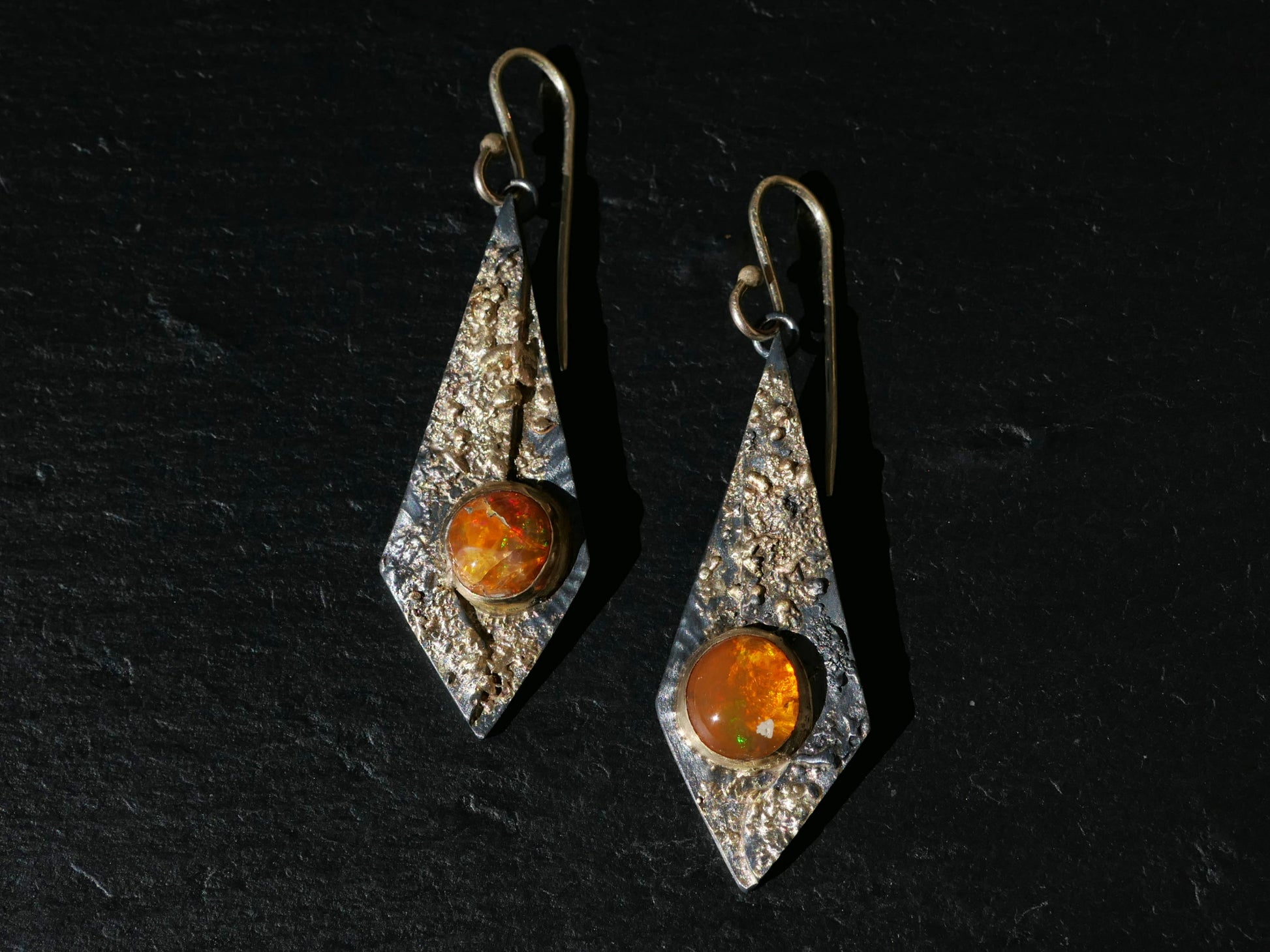 Kite-shaped statement earrings with orange Mexican fire opal gemstones set in textured 14k gold and black sterling silver, featuring 14k gold ear hooks.