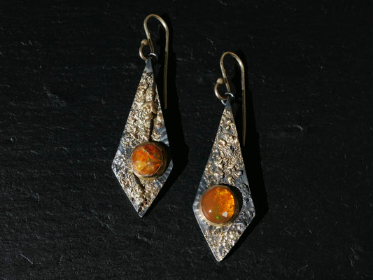 Kite-shaped statement earrings with orange Mexican fire opal gemstones set in textured 14k gold and black sterling silver, featuring 14k gold ear hooks.