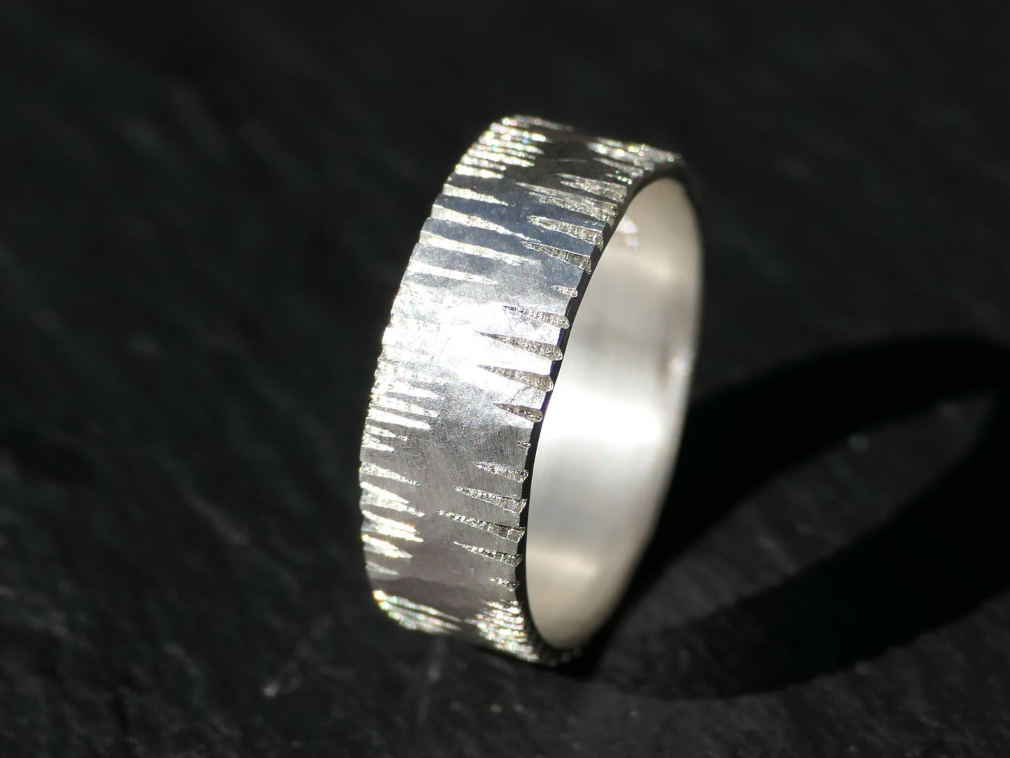 Minimalist handmade sterling silver wedding band with hammered texture and carved details, satin finish.