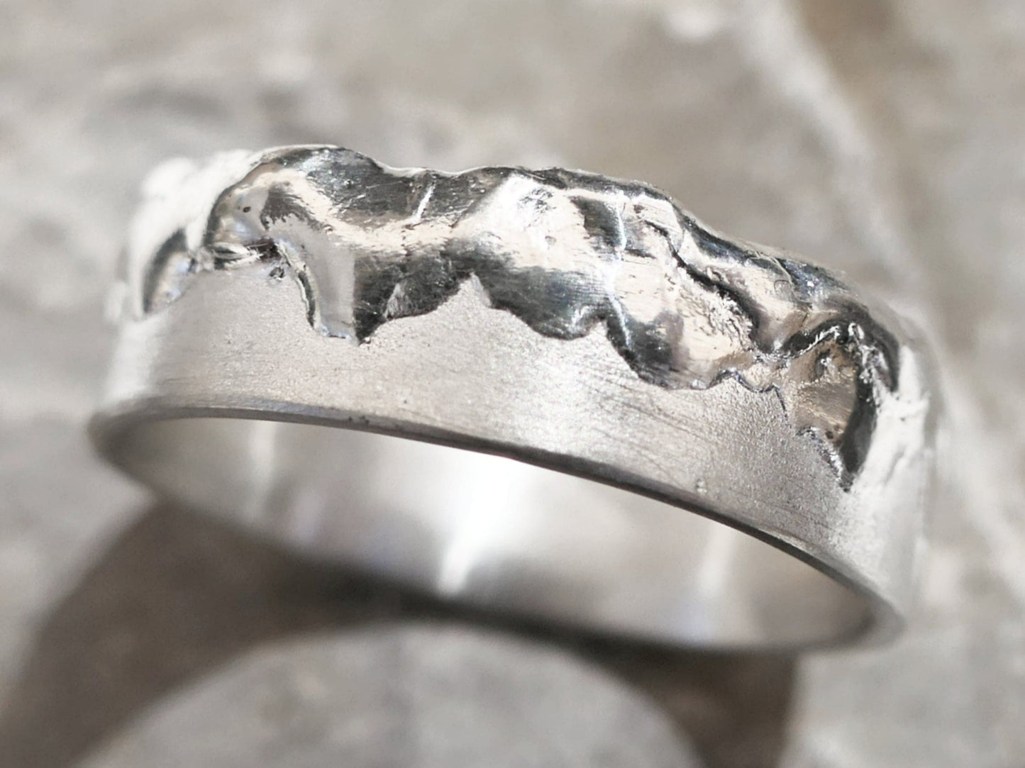 close-up of cool mens ring handcrafted from fine silver with partially molten textured surface and uneven edge