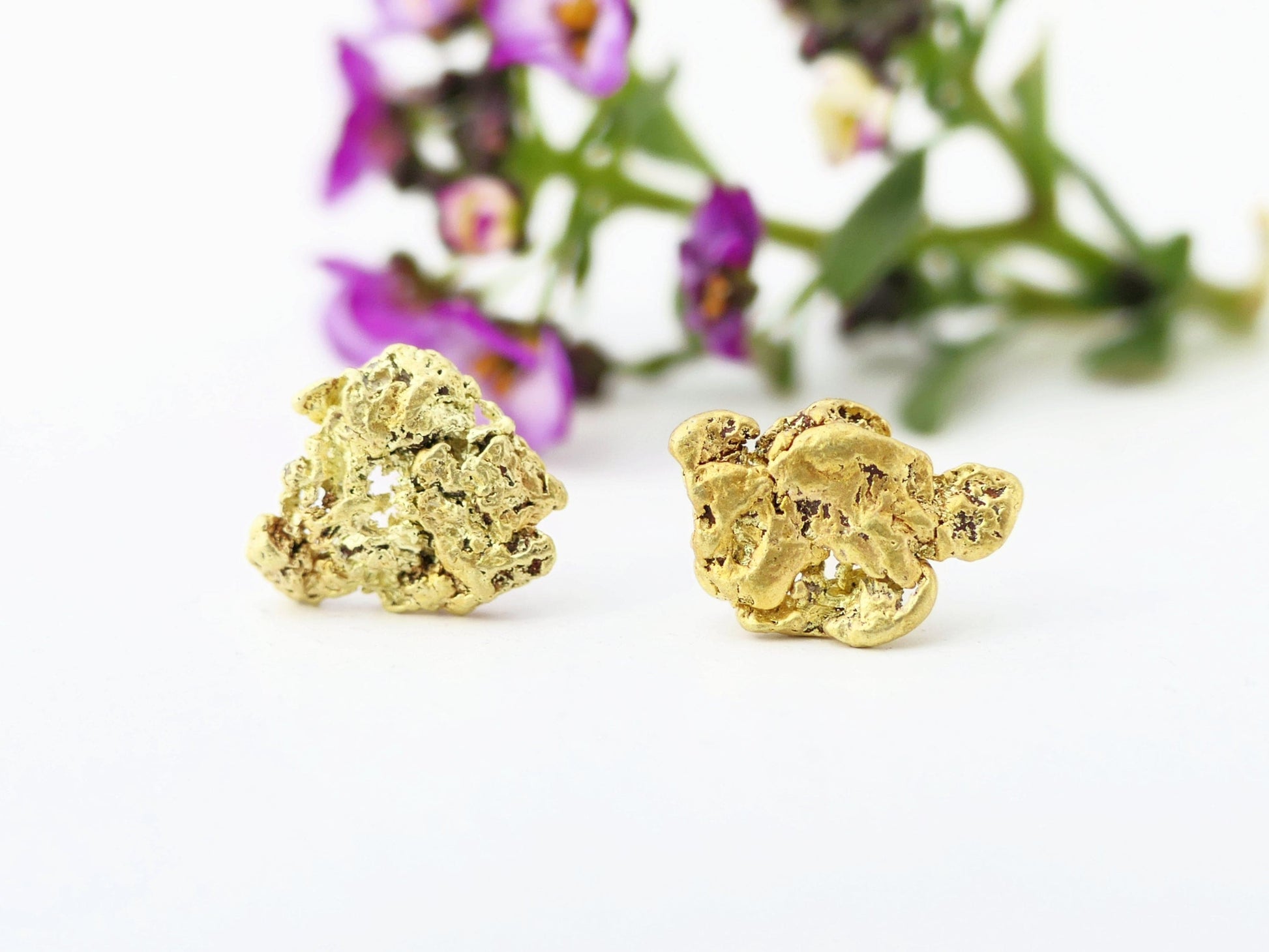 Natural all-natural Alaska gold nugget stud earrings with solid 14k yellow gold posts on white background with blurred purple flowers