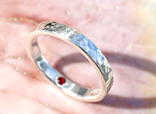 Hammered sterling silver ring with a hidden red gemstone inside the band.