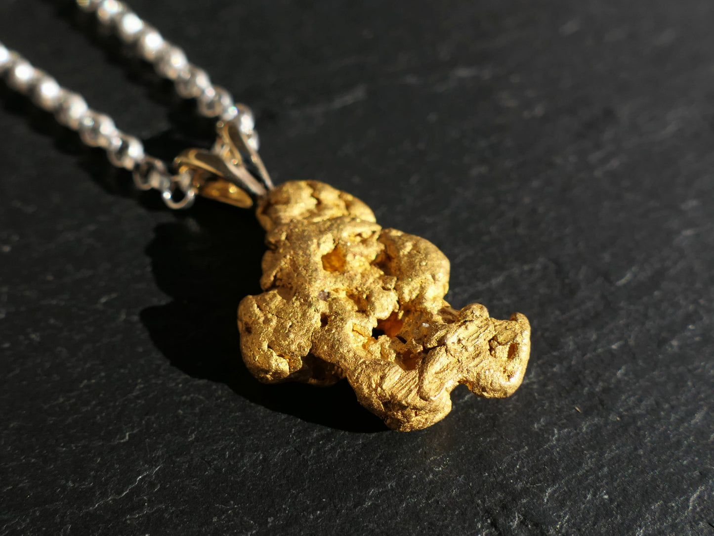 large raw gold nugget pendant with sterling silver chain on black surface