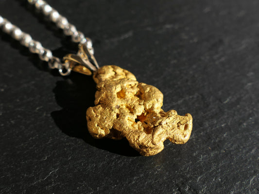 large raw gold nugget pendant with sterling silver chain on black surface