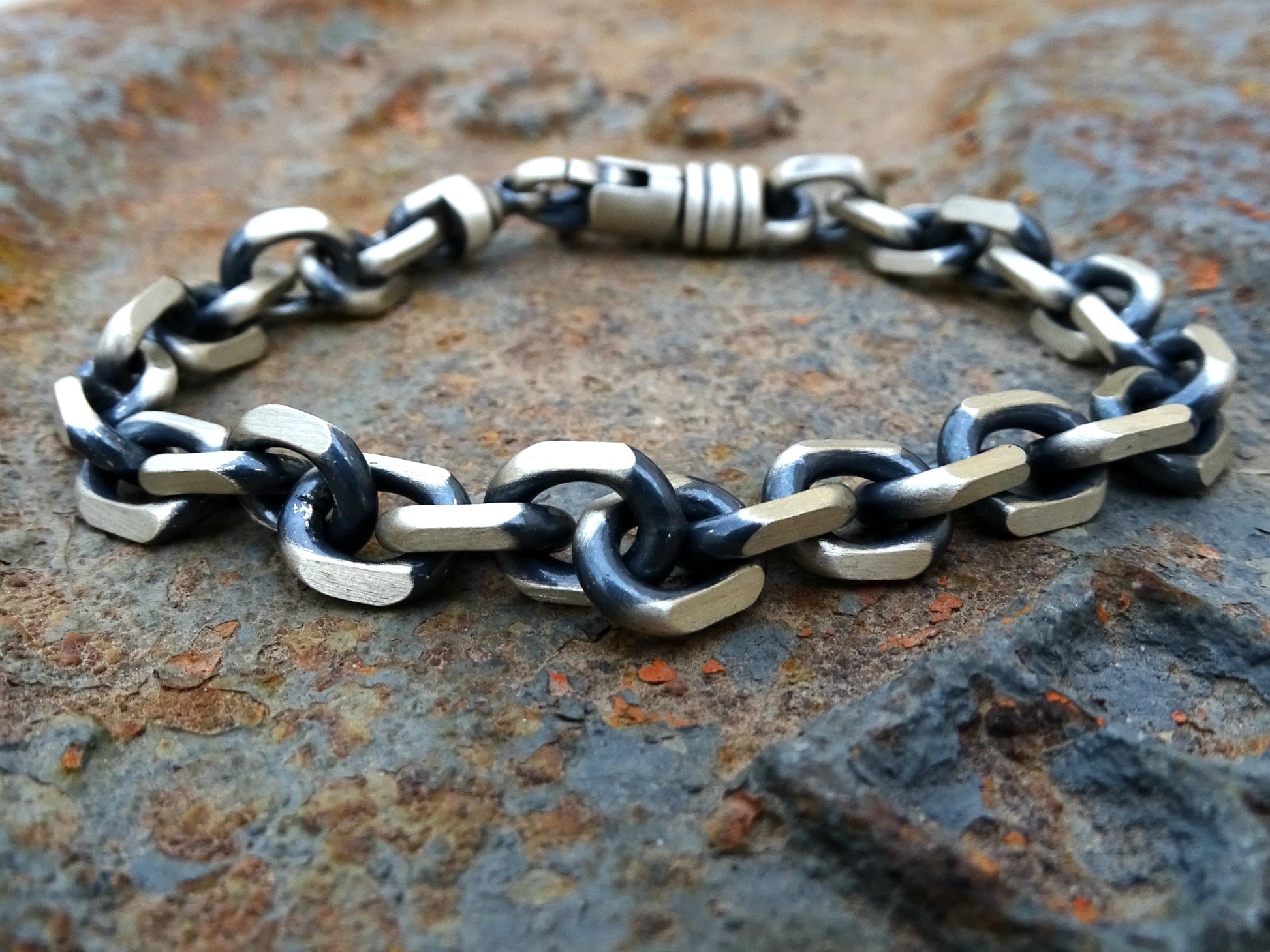 heavy men's sterling silver bracelet with large oxidized links and sturdy lobster clasp on rustic surface
