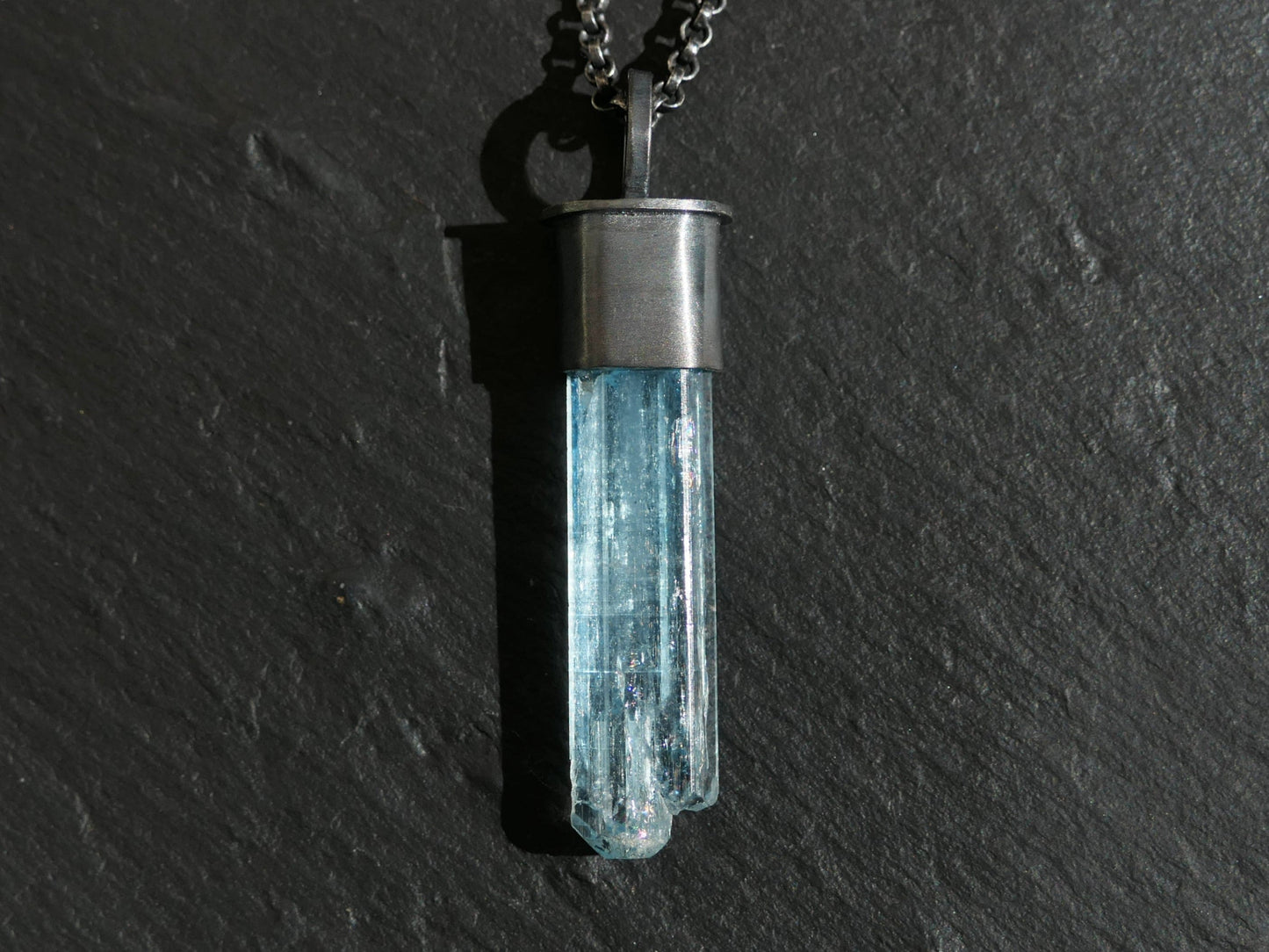 aquamarine crystal pendant with black sterling silver setting and chain on dark background