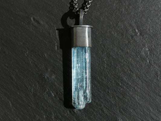 aquamarine crystal pendant with black sterling silver setting and chain on dark background