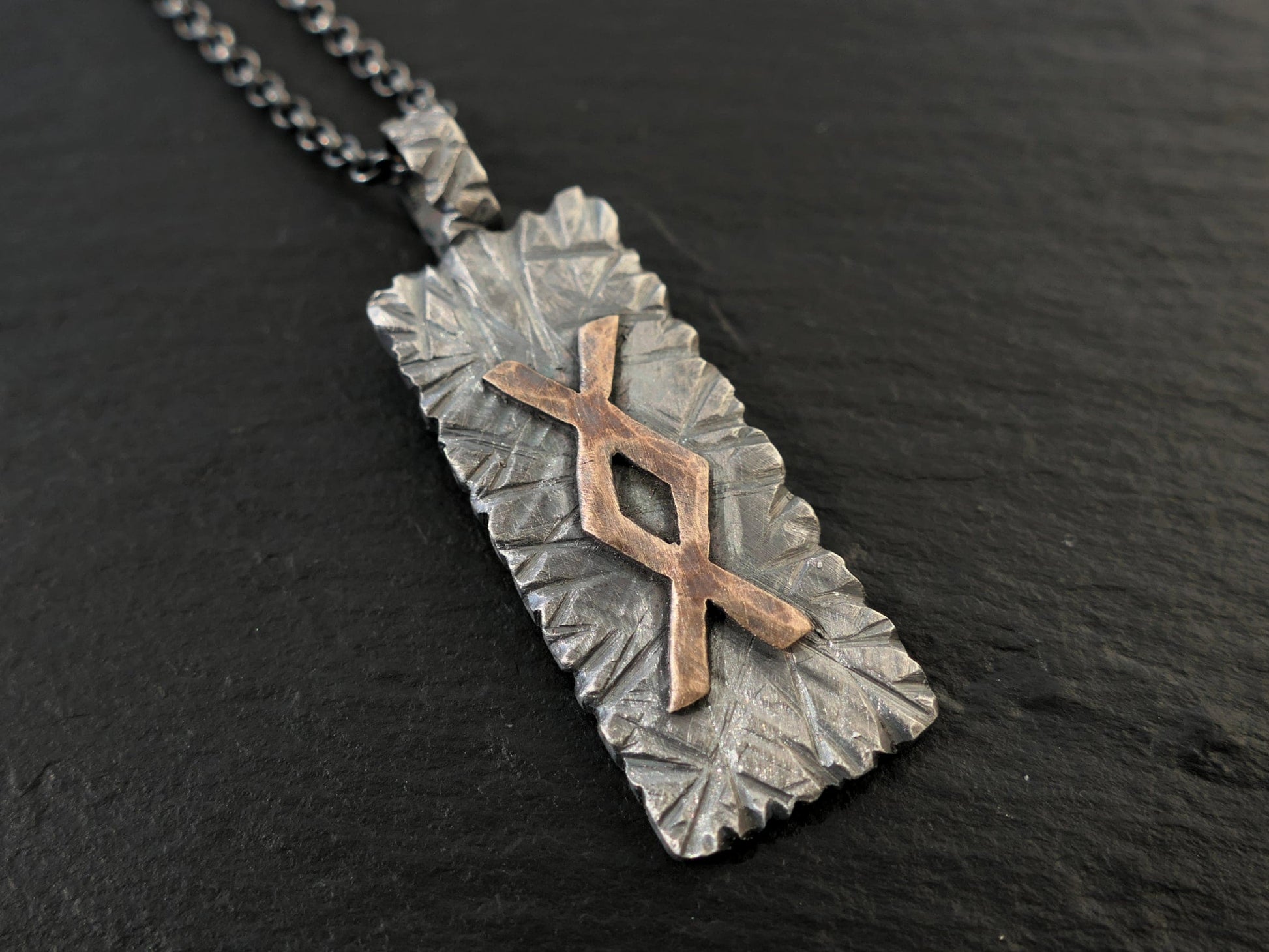 Darkened silver hand forged Nordic rune pendant with hammered bronze rune symbol on black chain