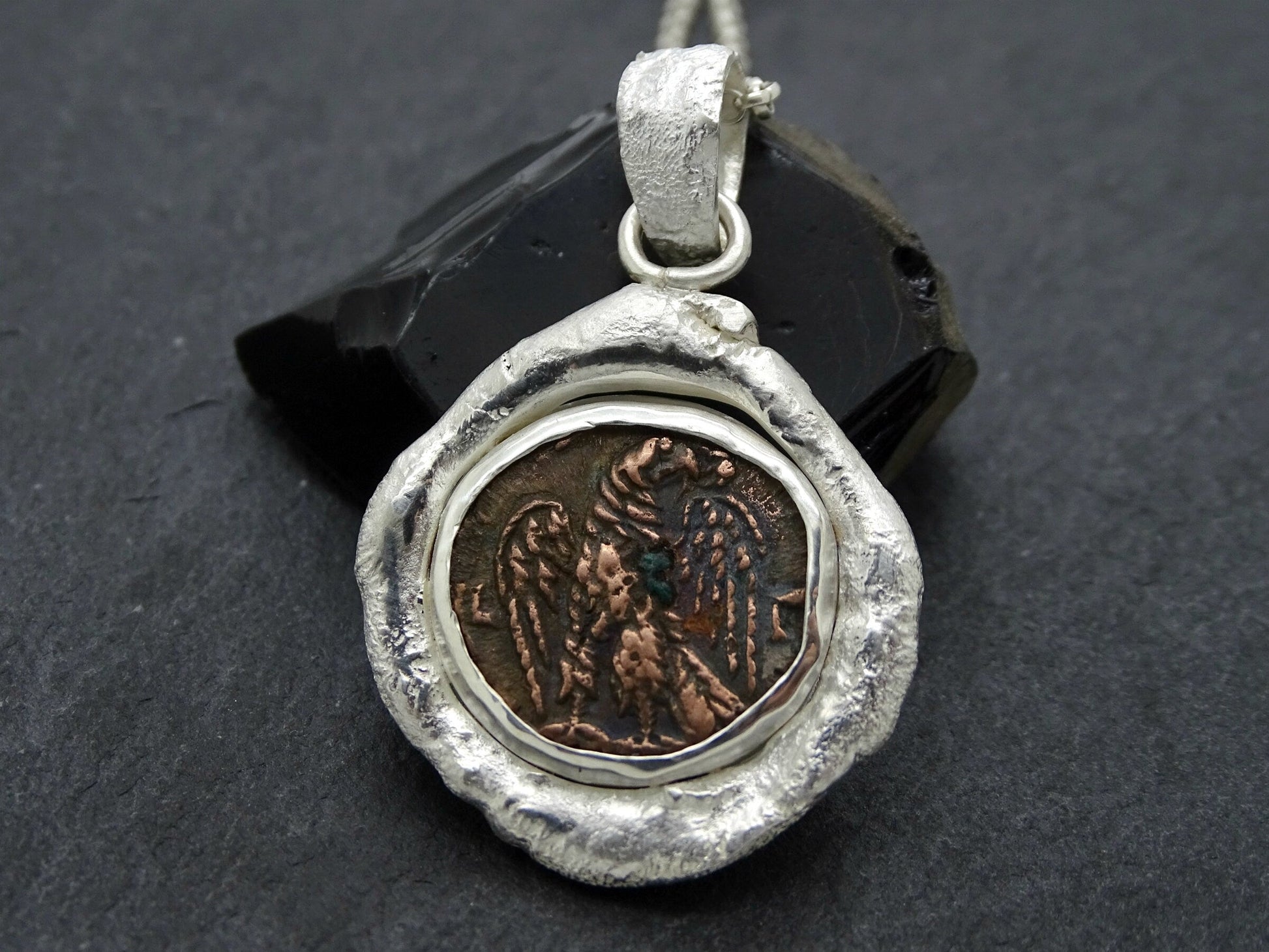 Close-up of a rustic silver Roman coin necklace pendant featuring an authentic ancient bronze coin with an eagle design from the Roman Empire.