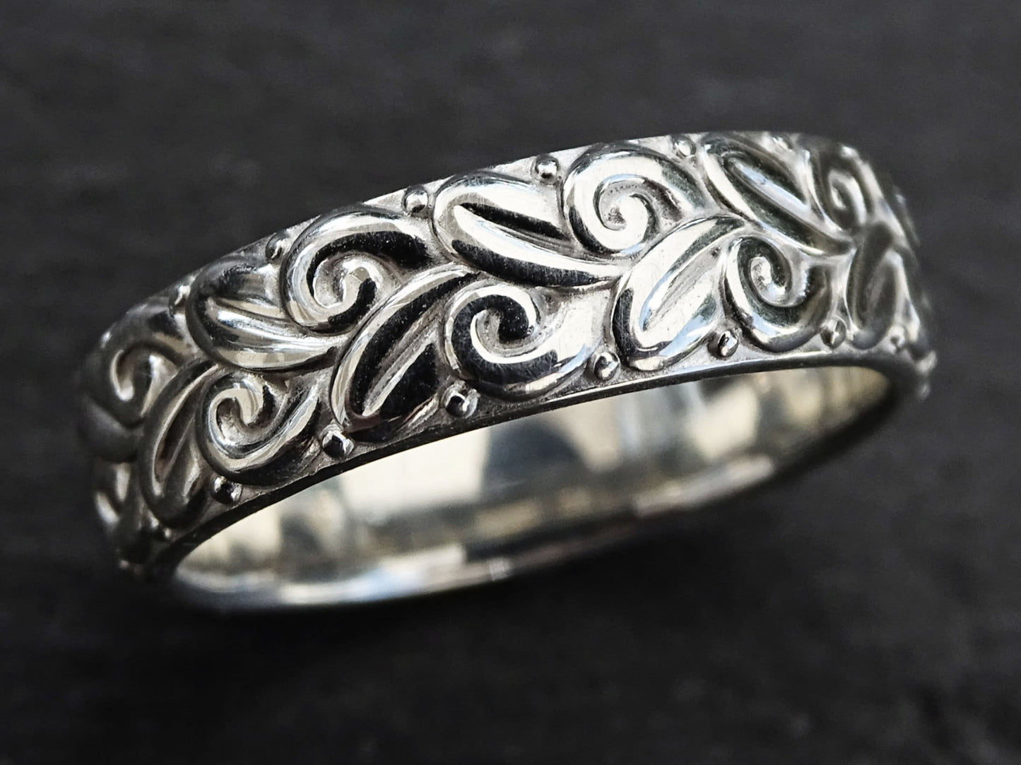 close-up of a sculptural sterling silver ring with a modern floral pattern and deep reliefs on a dark background