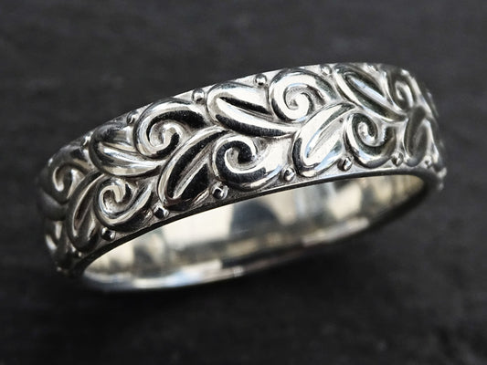 close-up of a sculptural sterling silver ring with a modern floral pattern and deep reliefs on a dark background