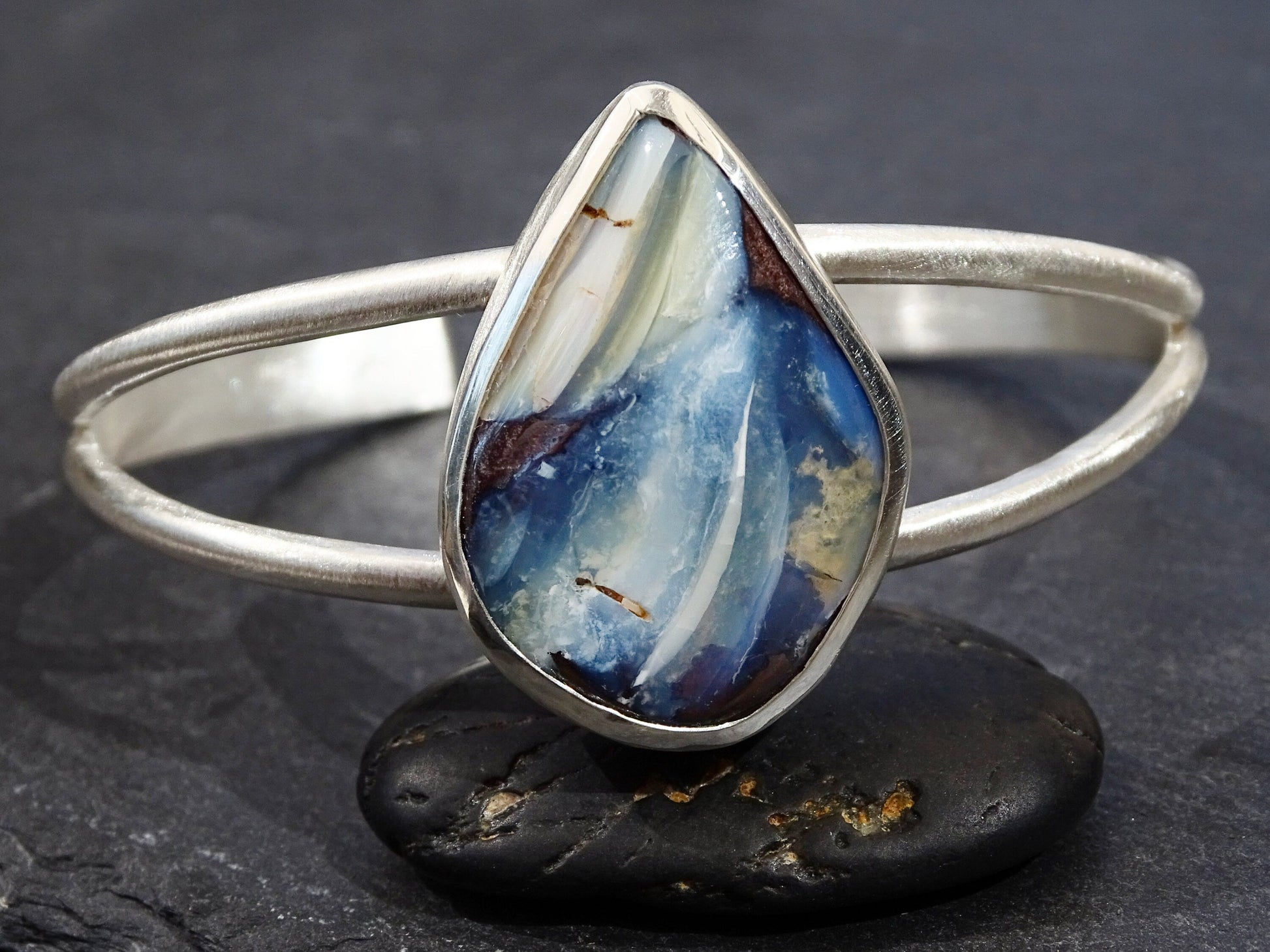 Unique blue boulder opal cuff bracelet in sterling silver with a teardrop-shaped natural opal stone set in a matte silver band
