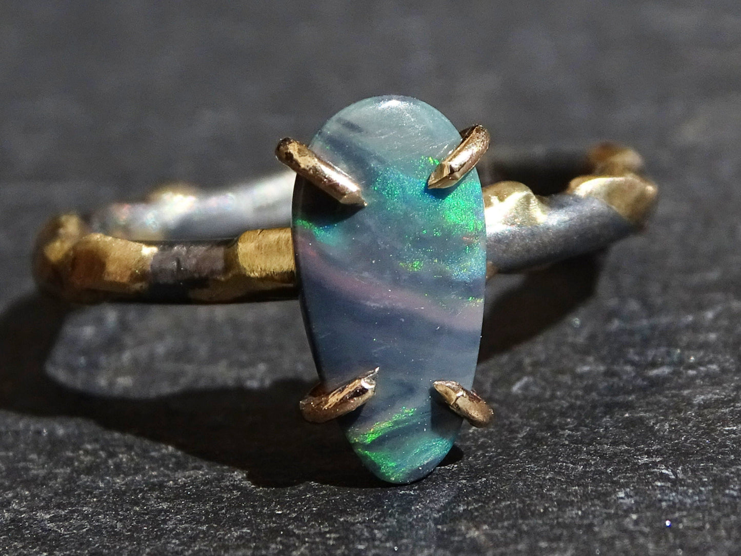 organic drop-shaped semi-black opal ring set in 14k yellow gold prongs on a black sterling silver band