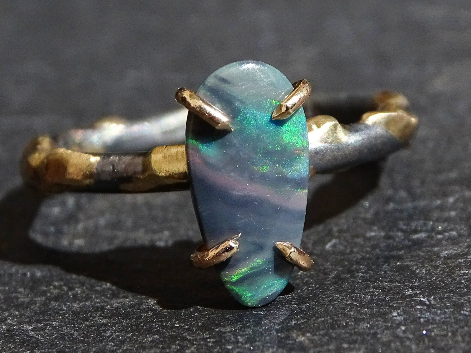 organic drop-shaped semi-black opal ring set in 14k yellow gold prongs on a black sterling silver band