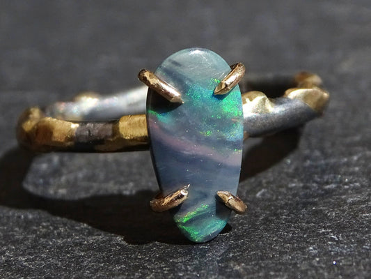 organic drop-shaped semi-black opal ring set in 14k yellow gold prongs on a black sterling silver band