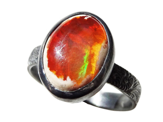 Red-orange fire opal ring with green and yellow flashes set in engraved black oxidized sterling silver band