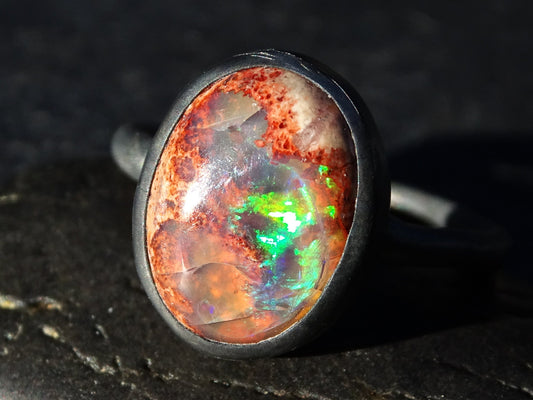 Oval natural fire opal engagement ring with blue and green flashes set in dark silver molten band