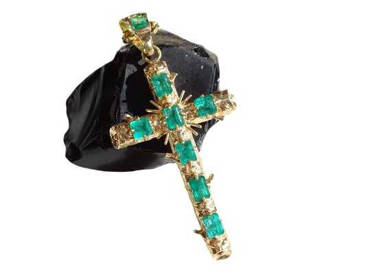 Large 18k gold cross pendant adorned with eight bright green Muzo emerald gemstones displayed on a black stone.