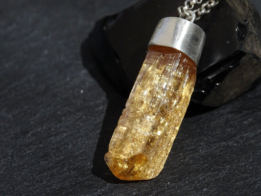 Imperial Topaz crystal pendant with sterling silver setting and chain on dark background