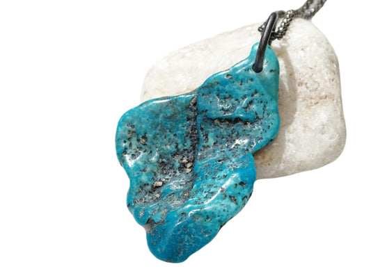 Large natural turquoise pendant with black silver bail on white stone background