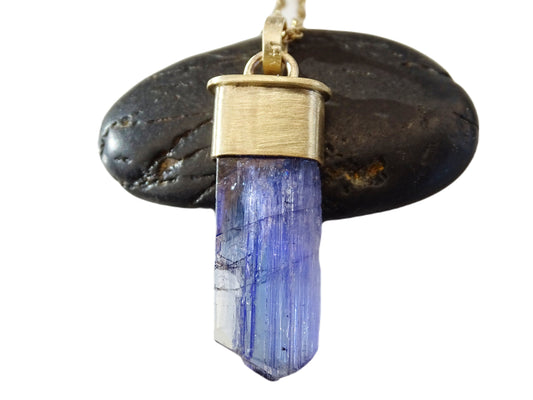 Unheated tanzanite pendant with raw blue-purple crystal set in 14k gold on black background