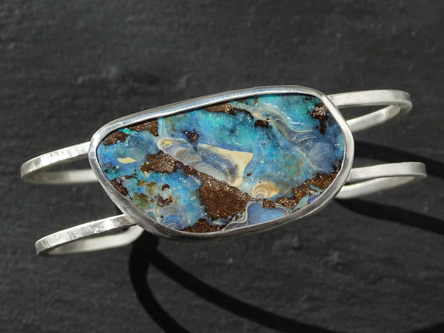 Large Australian boulder opal cuff bracelet in sterling silver with blue-green opal and earth-toned matrix stone in a closed bezel setting.