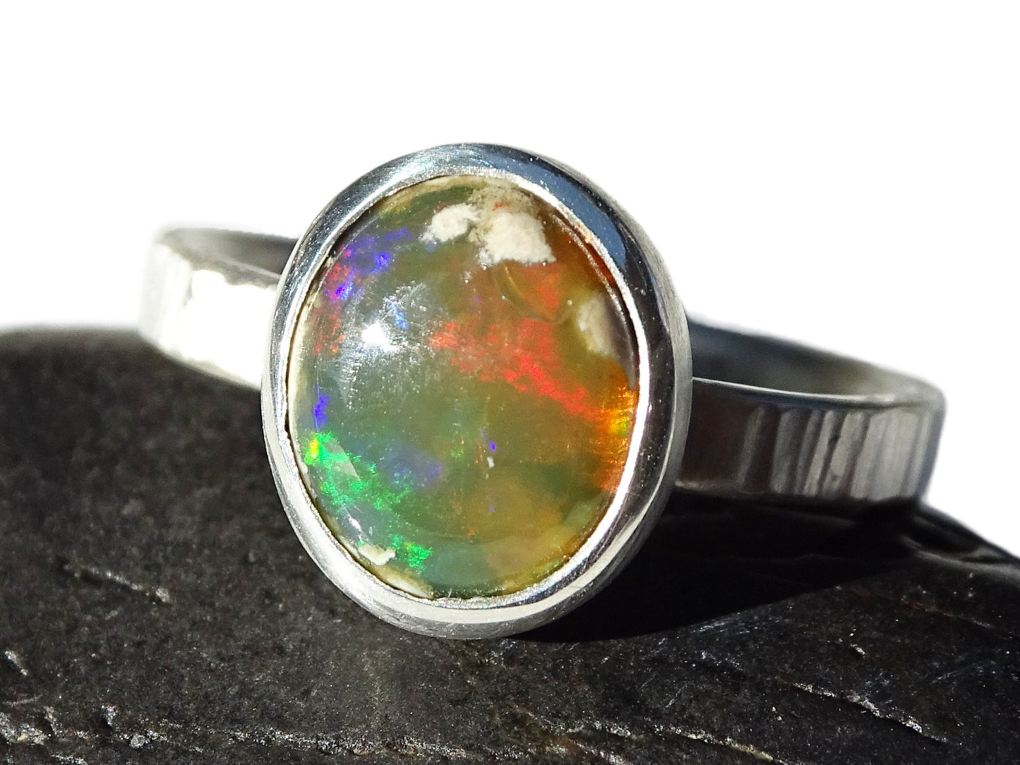Mexican fire opal ring with hammered silver band and closed bezel setting showing green, orange, and red play of color.