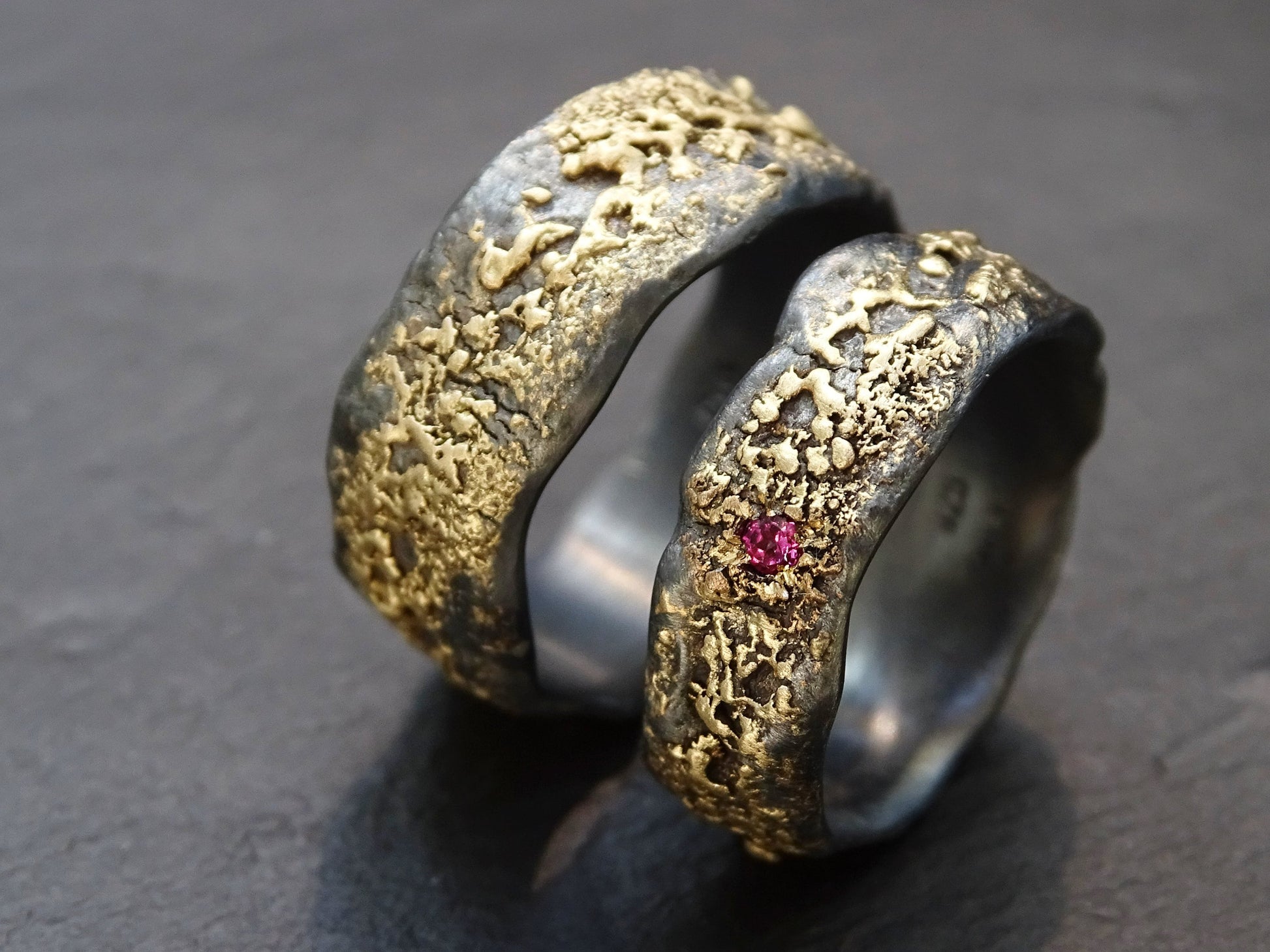 wedding ring set his and hers 14k gold textured over black sterling silver with a flush red gemstone on slimmer band